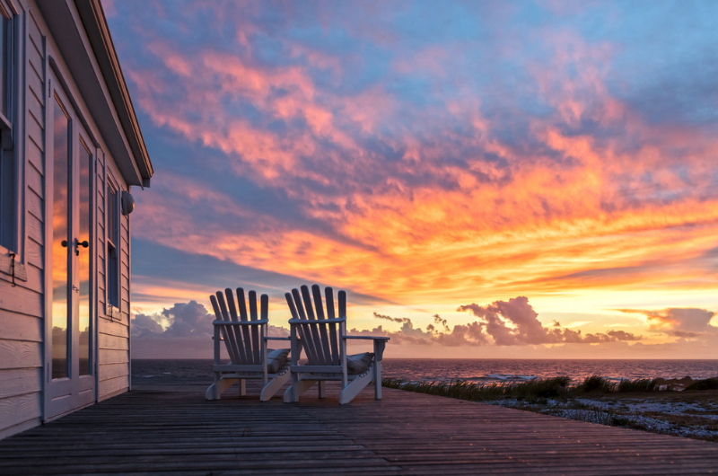 Picture of two empty beach chairs overlooking the sunset filled sky. 